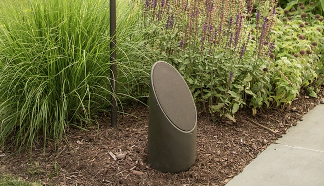 Durable outdoor speaker system positioned beside a walkway and garden plants for immersive outdoor audio.