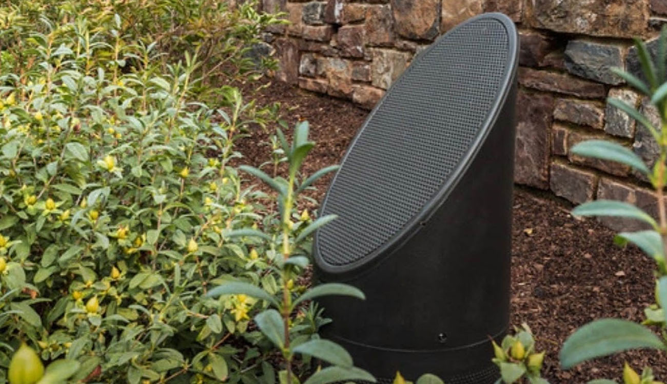 Weatherproof outdoor speaker system blending into landscape design near a stone wall and plants.