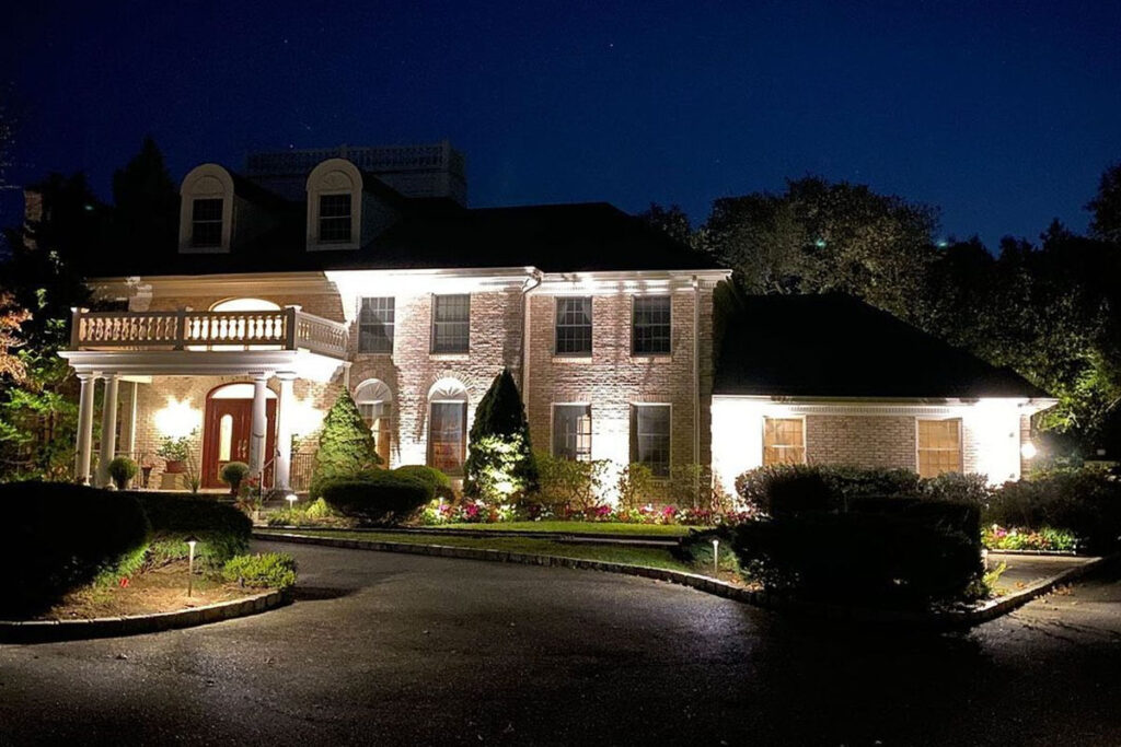 Brick home illuminated with architectural landscape lighting fixtures that highlight the home’s details and create a welcoming nighttime view.