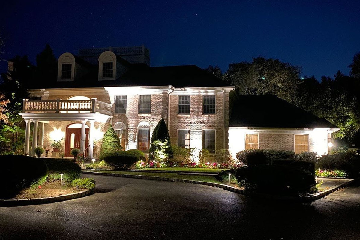 Brick home illuminated with architectural landscape lighting fixtures that highlight the home’s details and create a welcoming nighttime view.