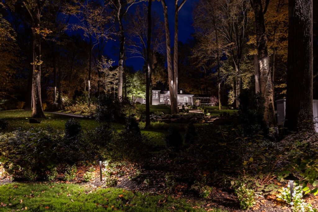 Luxury Garden Lighting Ideas showing a beautifully illuminated home and landscape with soft accent lights highlighting trees and pathways at night.