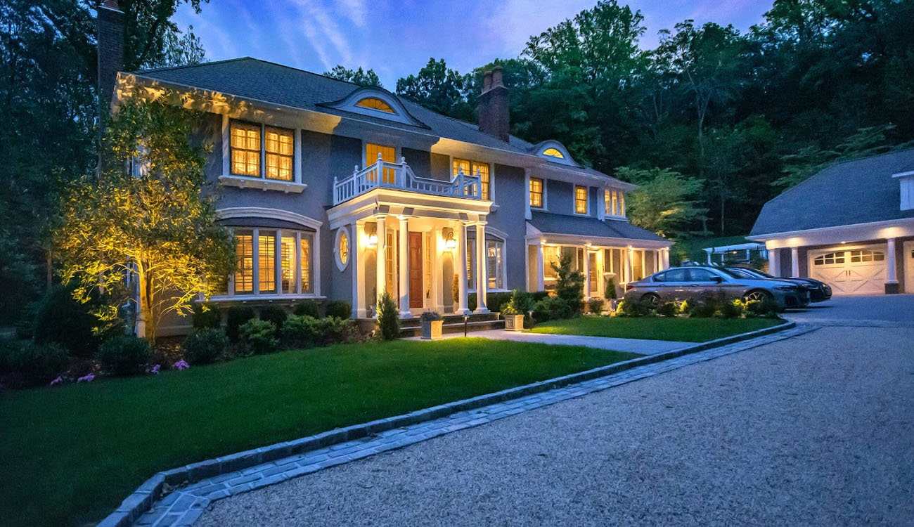 Front Yard Landscape Lighting Tips to Boost Curb Appeal in Mill Neck, NY 4 Front yard landscape lighting illuminating a two-story home, entryway, and trees during early evening.