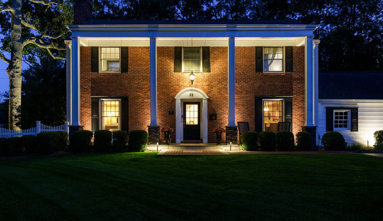 How Much Does Outdoor Lighting Installation Cost in Massachusetts? 4 Colonial-style brick home lit with pathway and façade lighting, an example used to understand outdoor lighting installation cost in Massachusetts.