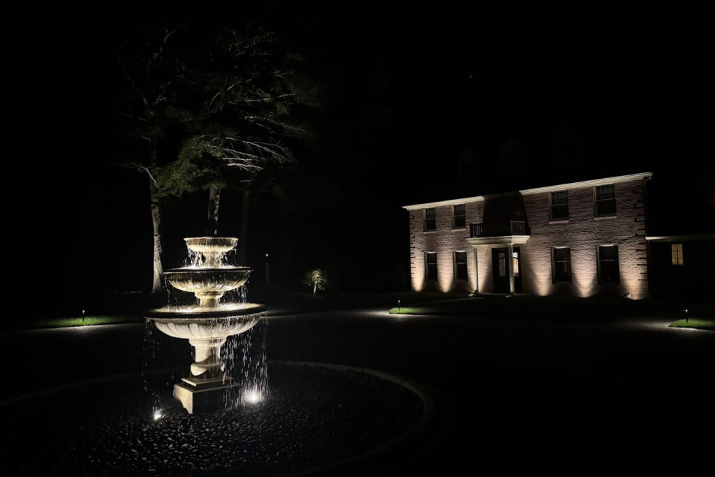 Elegant front yard with a lit fountain and home façade showcasing professional architectural lighting in Norfolk County.