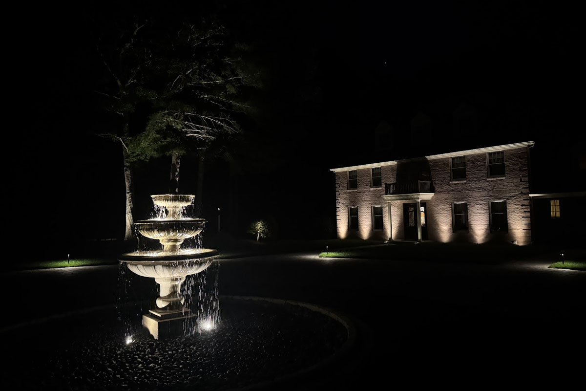 Elegant front yard with a lit fountain and home façade showcasing professional architectural lighting in Norfolk County.