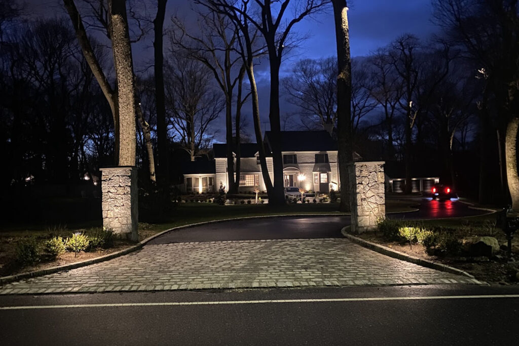 10 Reasons Why LED Landscape Lighting Is Worth It 10 A large home sits beyond a lit driveway and tall trees, where LED Landscape Lighting brightens the entrance and adds safety to the nighttime scene.