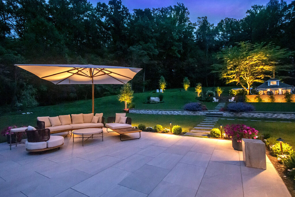 Mistakes to Avoid When Installing Low Voltage Landscape Lighting 1 A modern patio glows with soft garden lights and a large umbrella, showing how Low Voltage Landscape Lighting creates a warm, welcoming outdoor space.